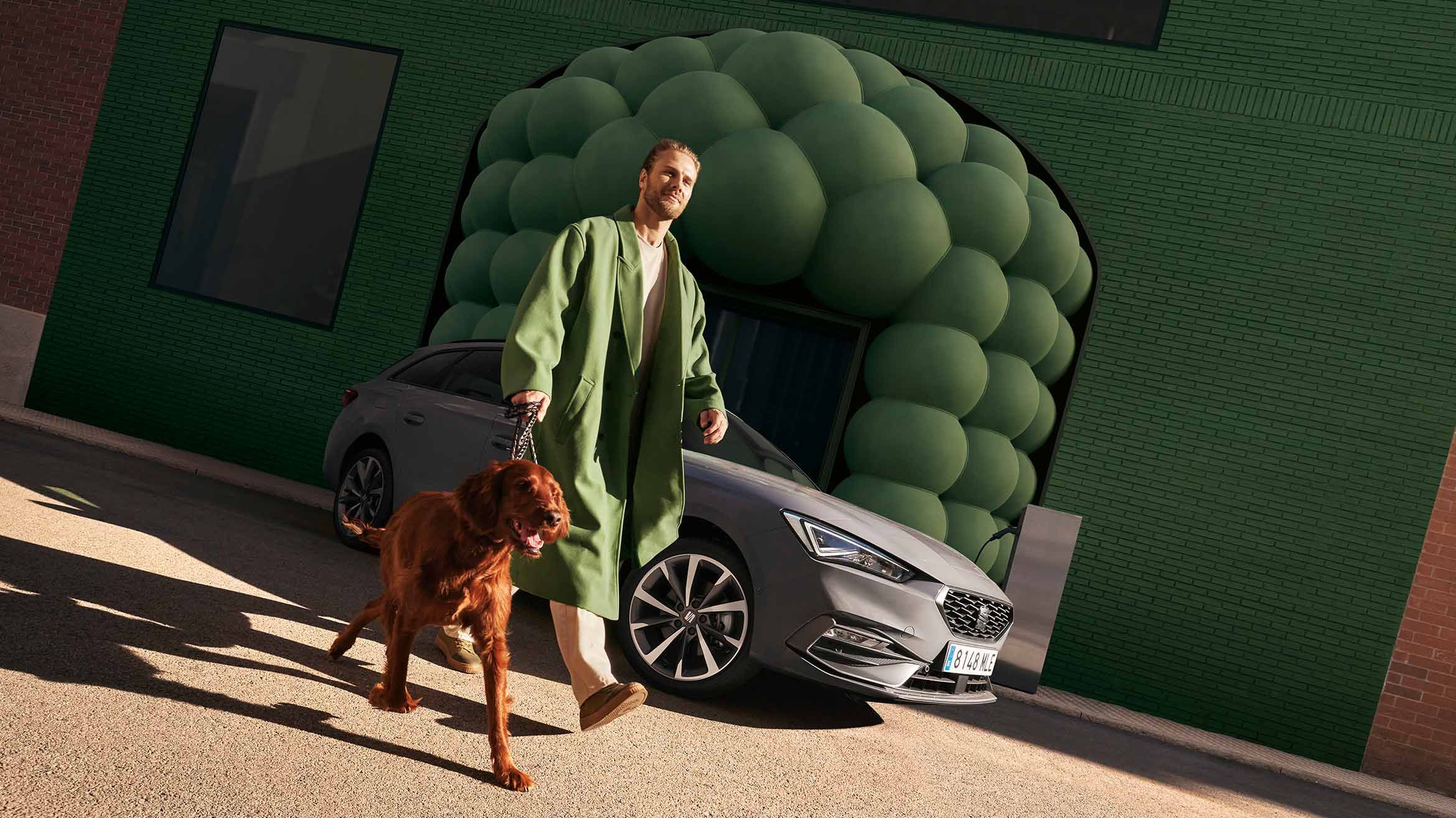 man walking with a dog past a grey seat leon sportstourer fr 2024 with cosmo grey machined alloy wheels on a city street