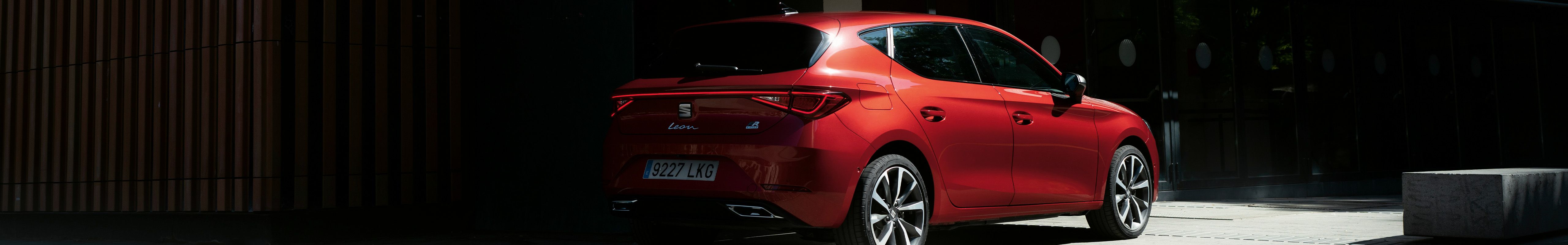 Mild hybrid electric vehicle seat leon sportstourer in red parked in the shadows by a building