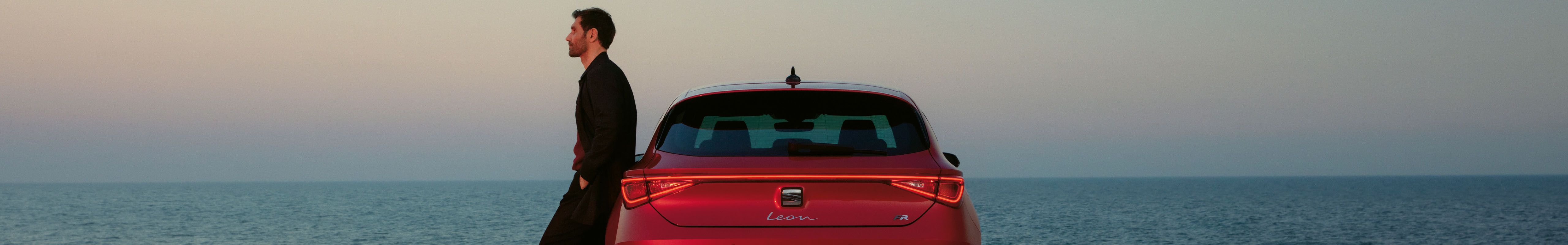 Plug in hybrid electric vehicle seat leon in red, rear view lights, sunset and sea